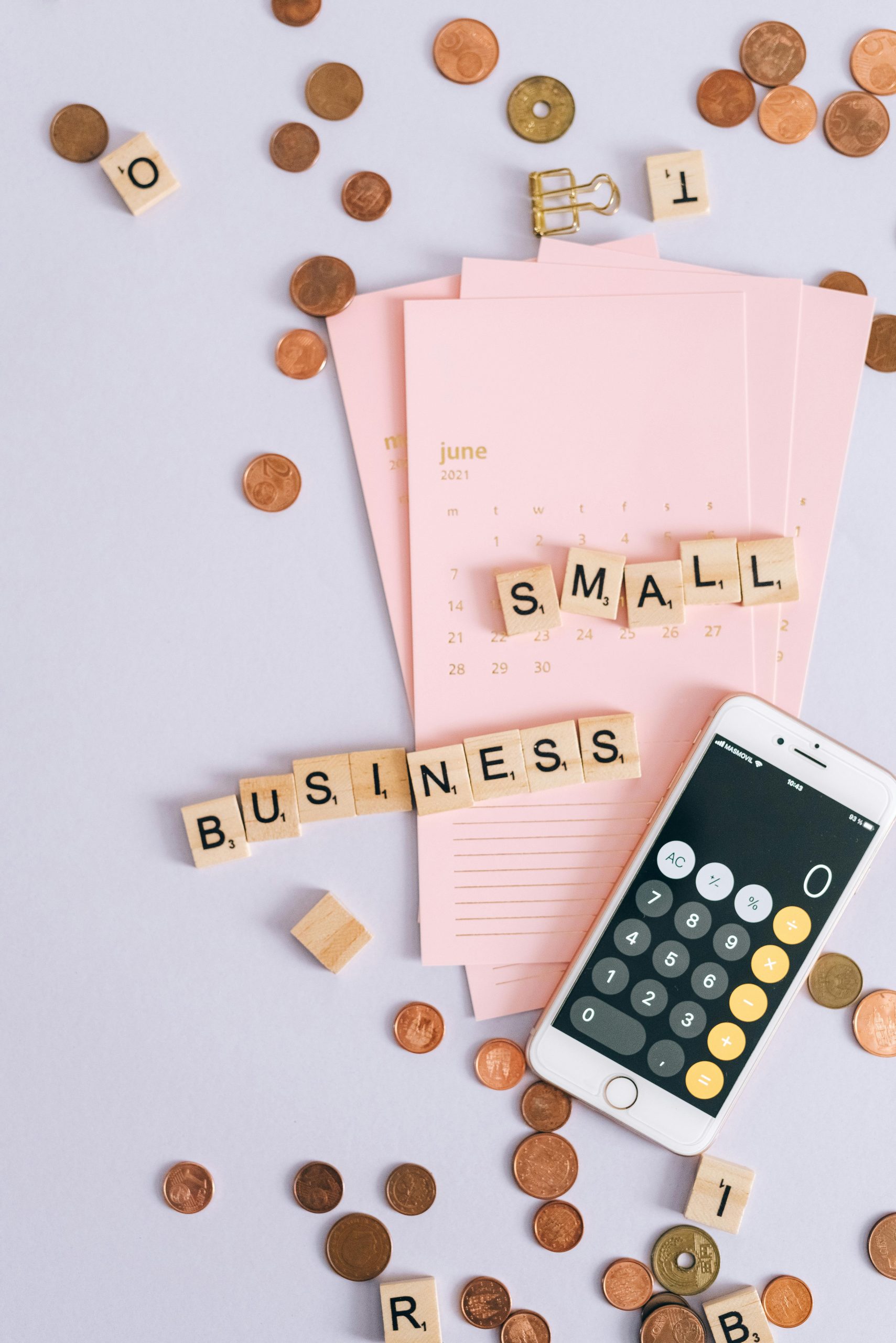 Small business planning setup with coins, calendar, and calculator alongside tiles spelling small business, representing the shift from effort-based income to structured, scalable digital assets that generate long-term value.