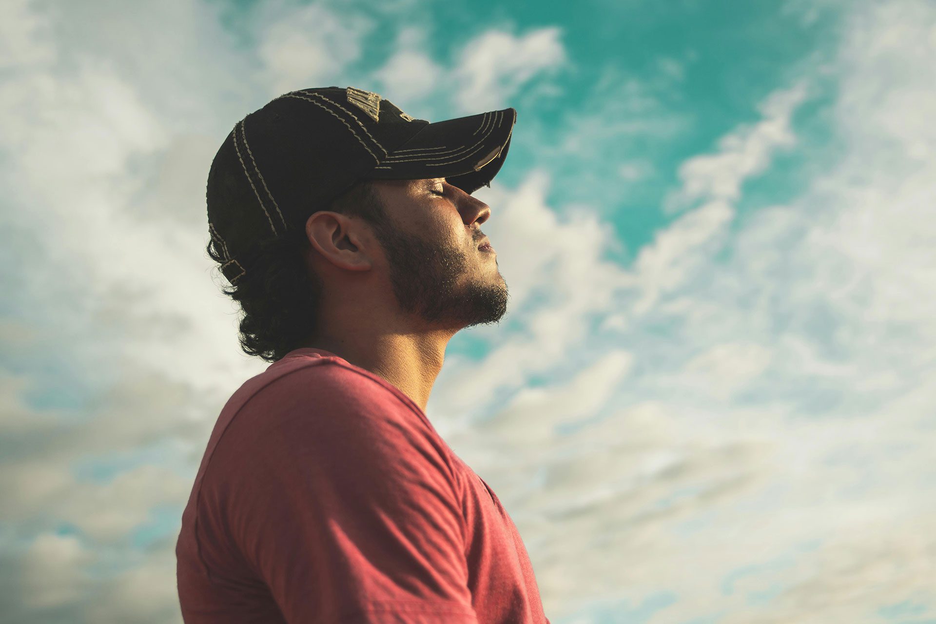 Side profile of a man in a cap looking upward into a bright blue sky with clouds, symbolising clarity and renewed focus.