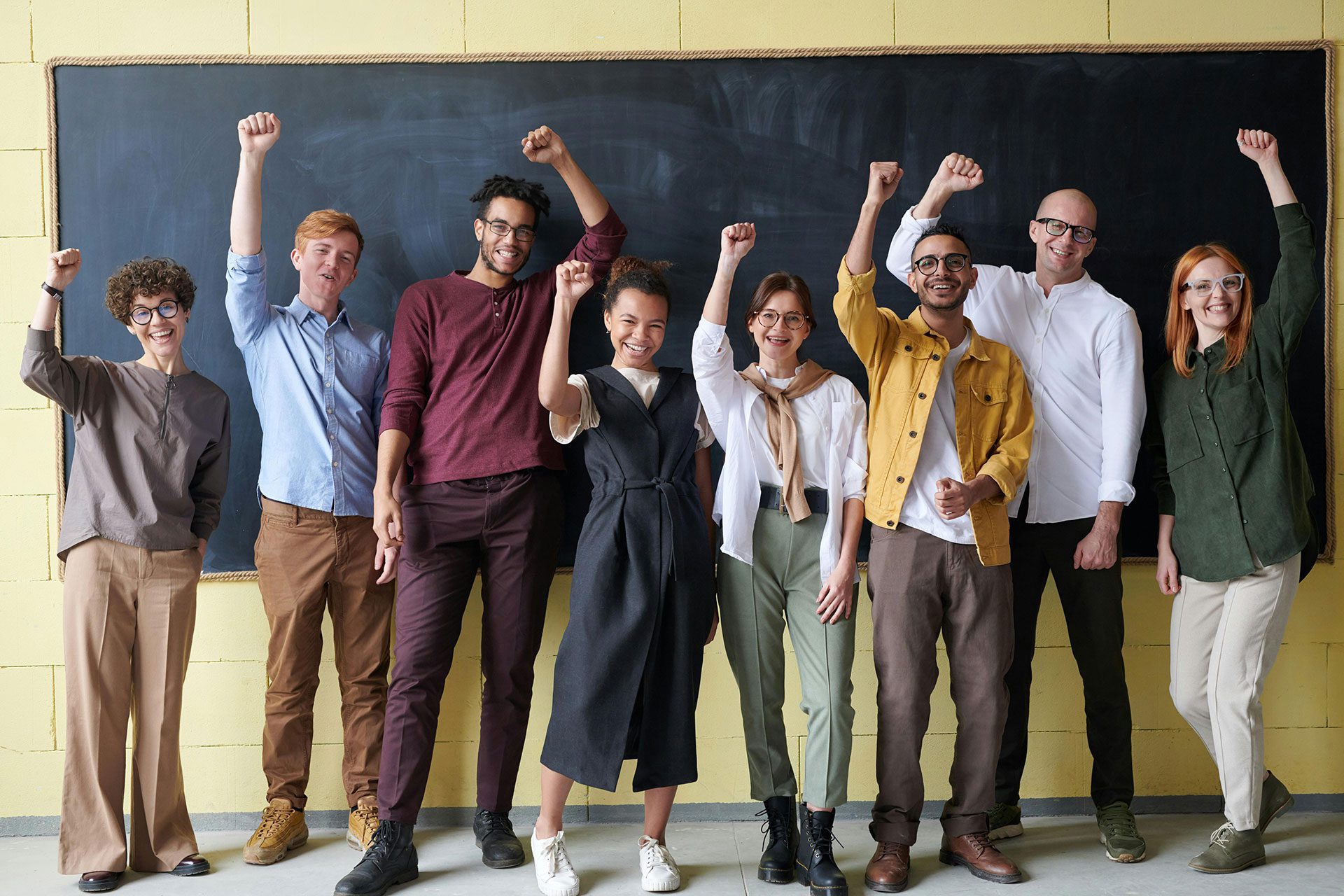 Diverse group of professionals smiling with raised fists in front of a chalkboard, representing business readiness, credibility, and investor confidence.