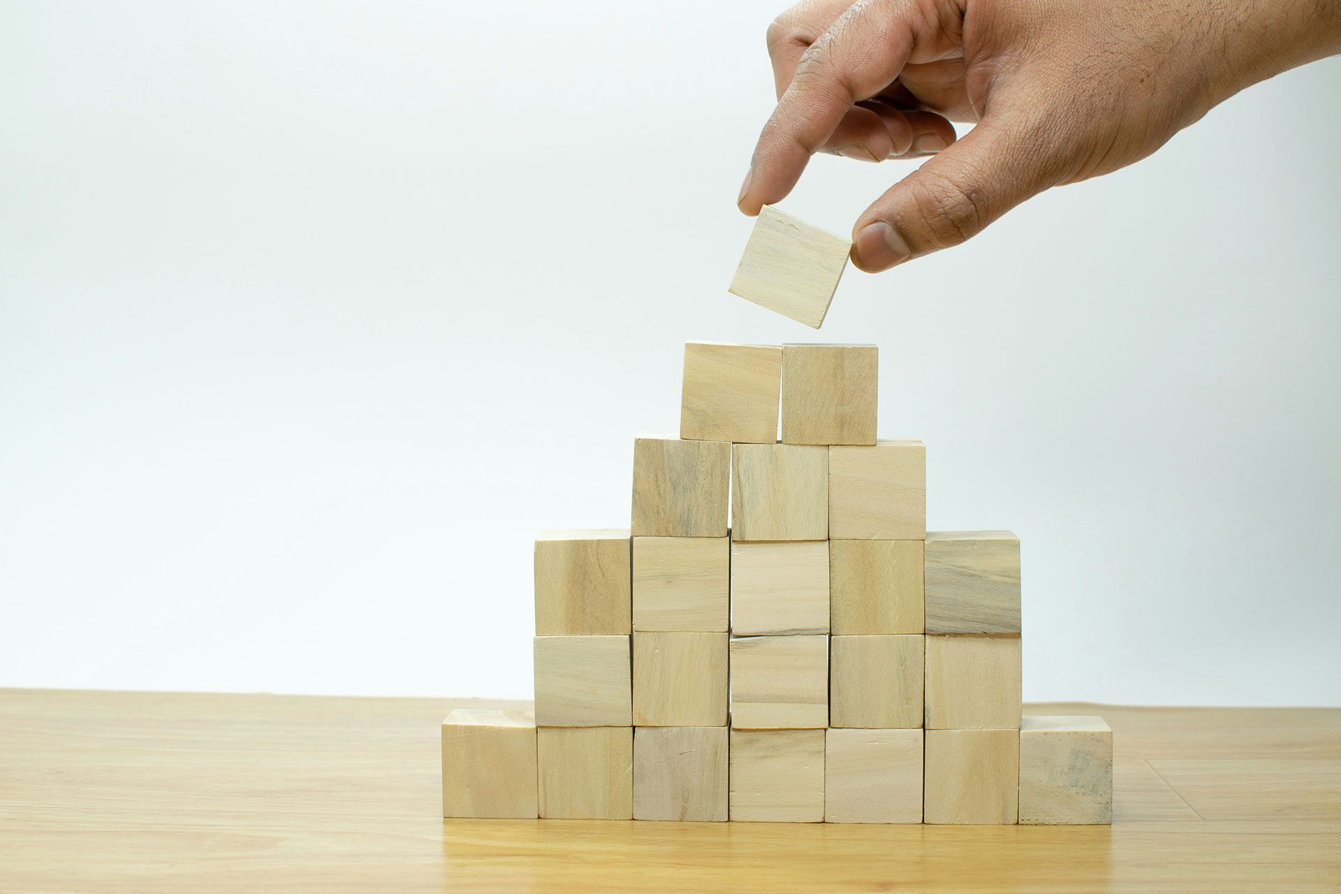 Hand placing a wooden block on top of a growing structure, symbolising how SMEs can build scalable systems, intellectual property, and compounding digital assets step by step over time.